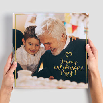 Deux personnes tiennent un album photo avec une couverture chaleureuse : 'Joyeux anniversaire Papy!'
