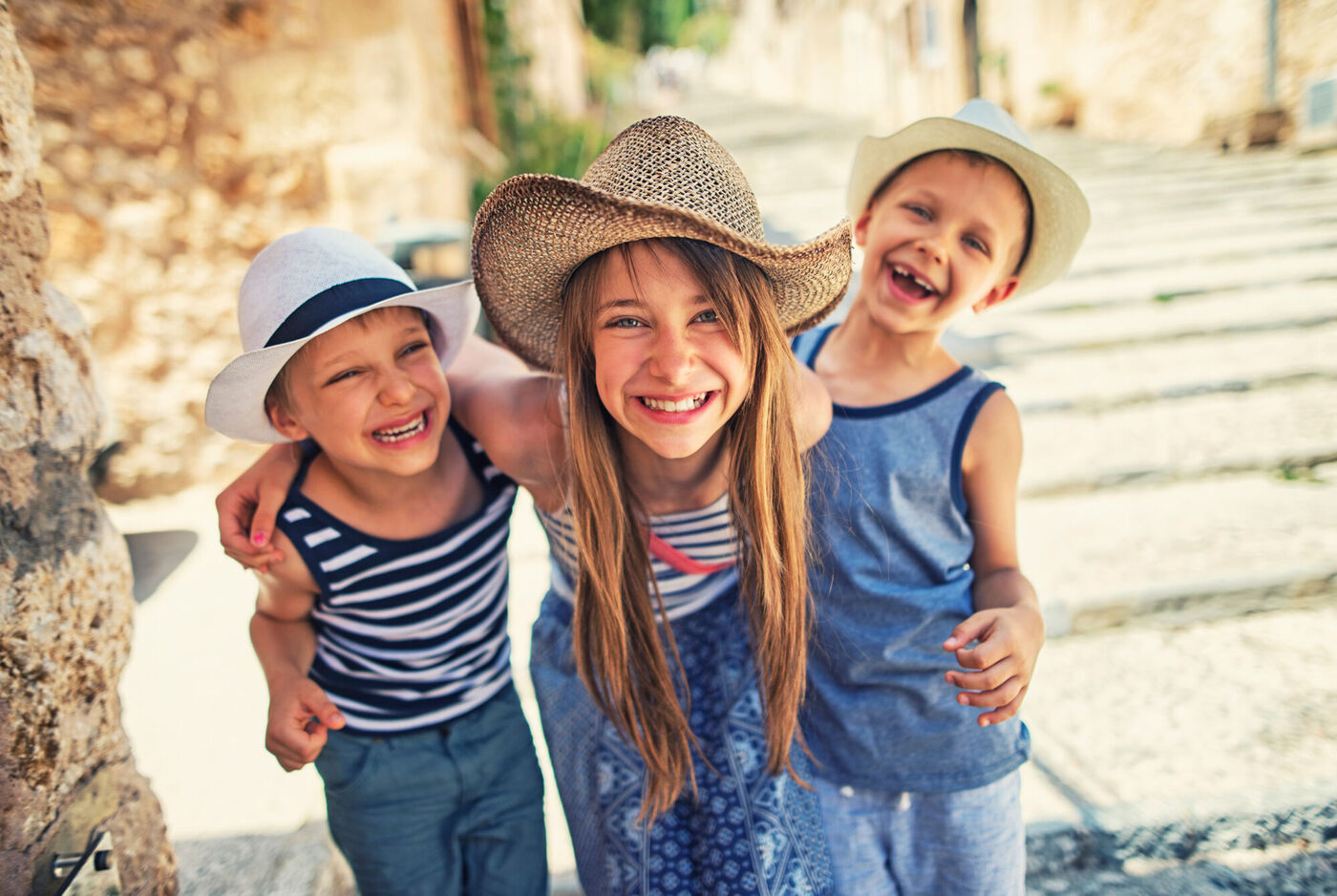 Trois enfants avec des chapeaux et un sourire joyeux dans une rue pittoresque