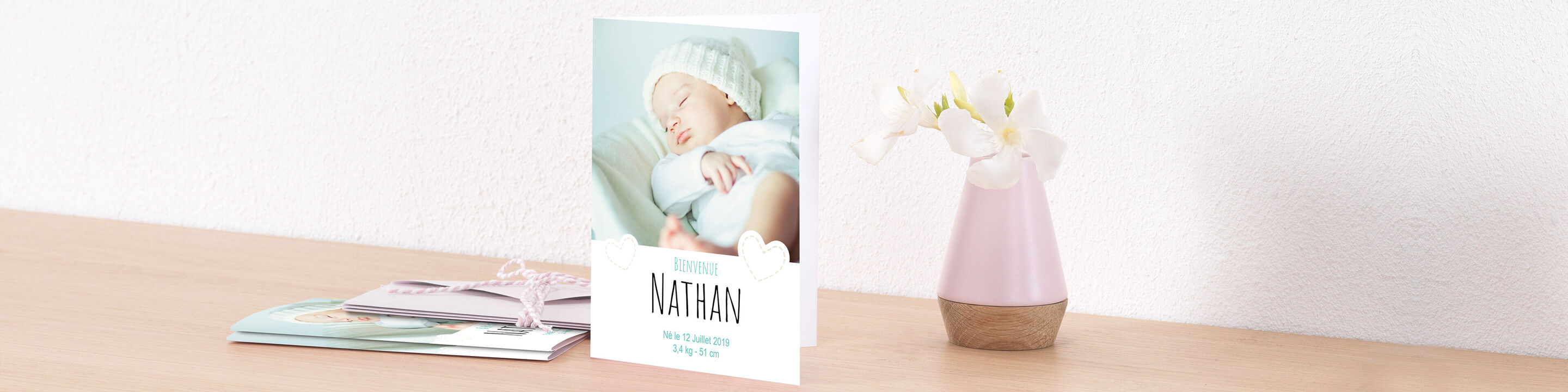 Une carte de vœux douce avec le nom Nathan et un bébé dormant, entouré de belles fleurs sur une table.