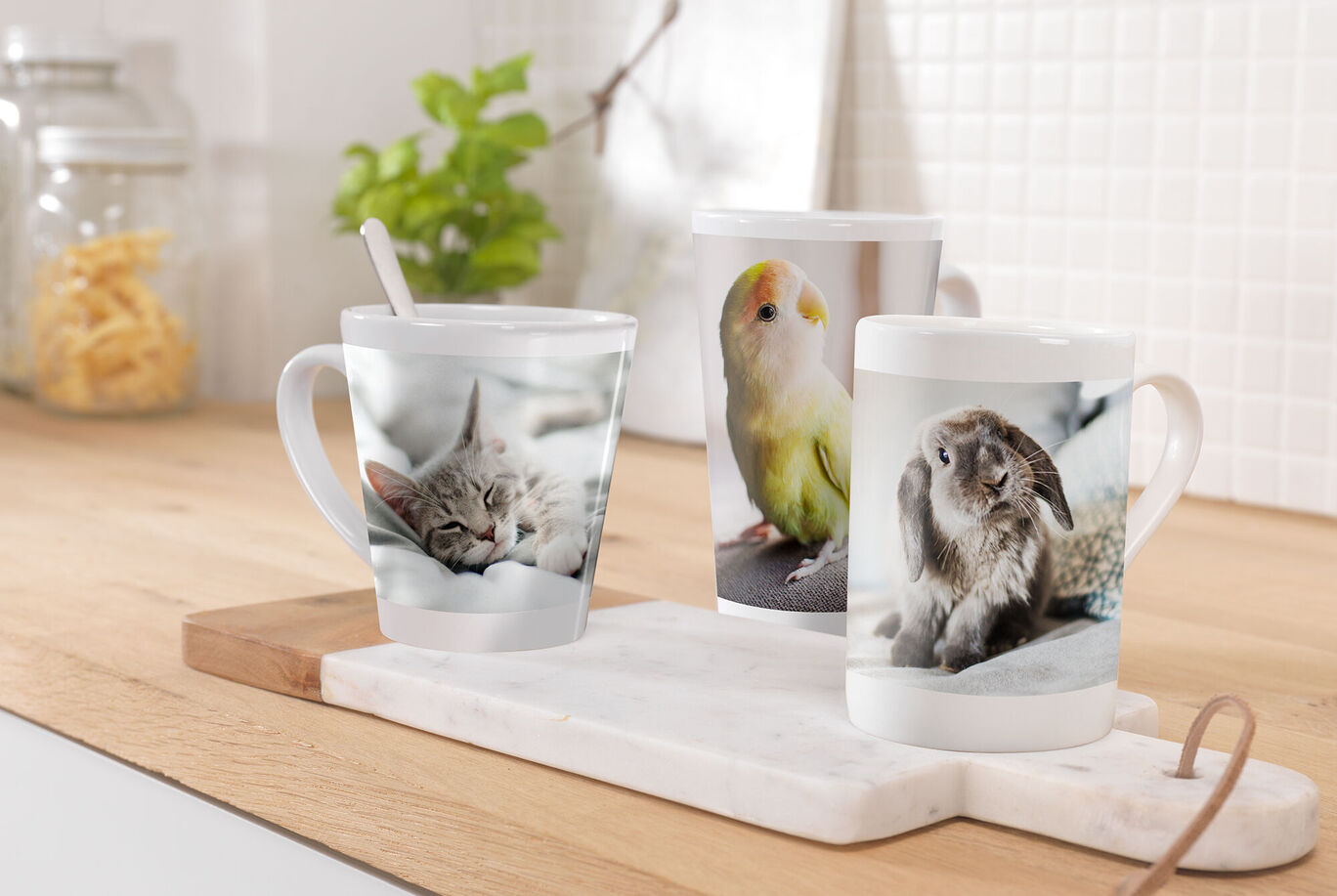 Trois tasses personnalisées sur un plateau en marbre dans une cuisine lumineuse, montrant des chats, un oiseau et un lapin.