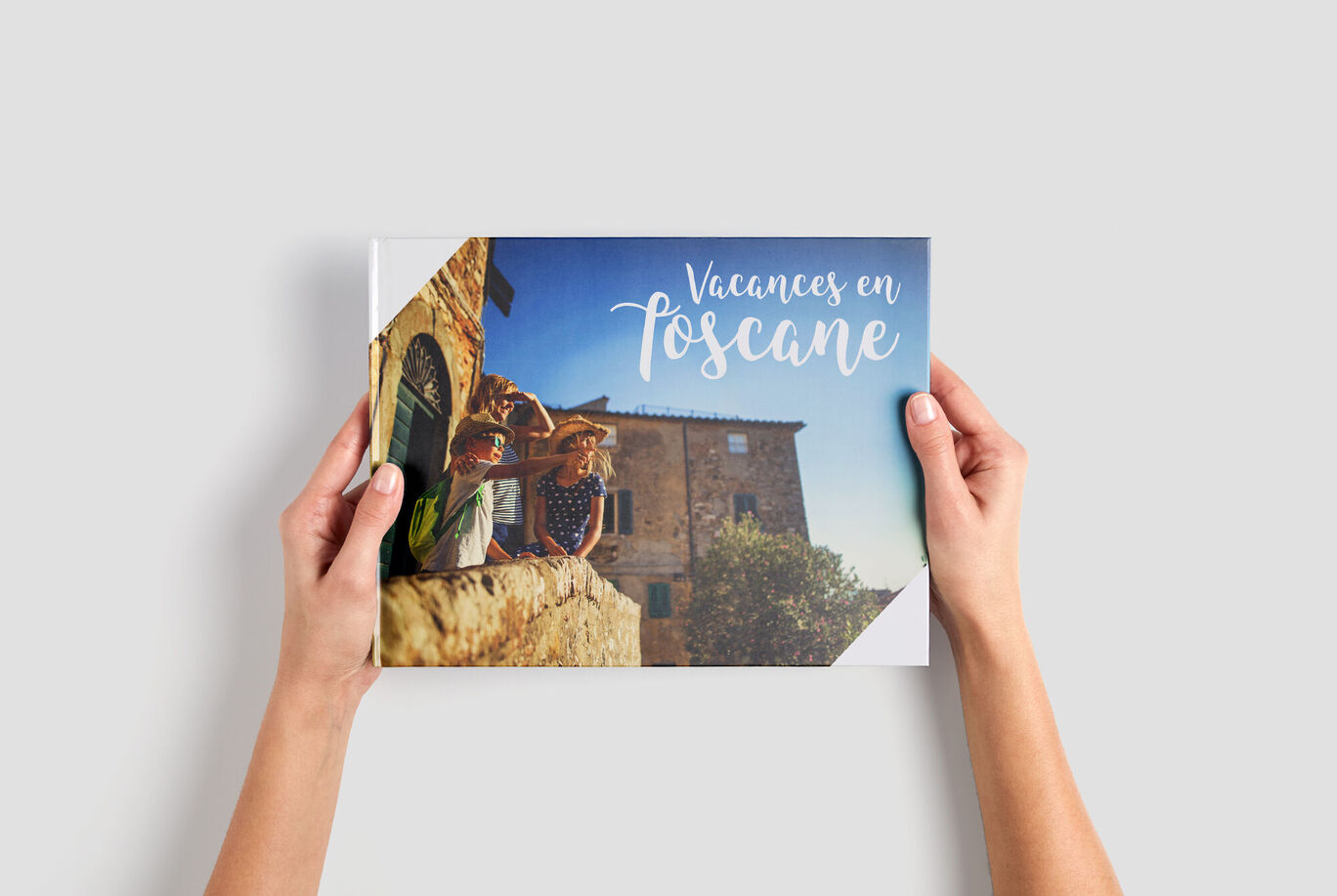 Deux personnes tiennent un CEWE ALBUM PHOTO intitulé 'Vacances en Toscane' devant un bâtiment historique.
