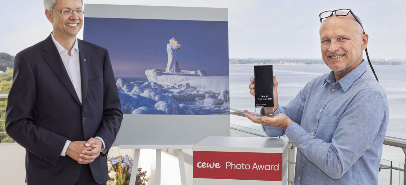 Deux hommes présentent le CEWE Photo Award devant une œuvre d'art.