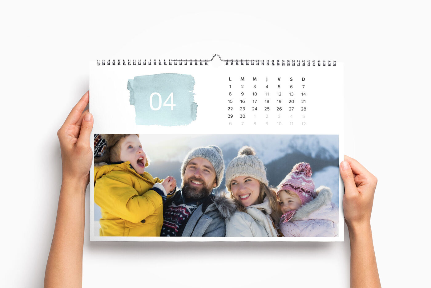 Des personnes tiennent un calendrier photo CEWE avec un beau motif hivernal.