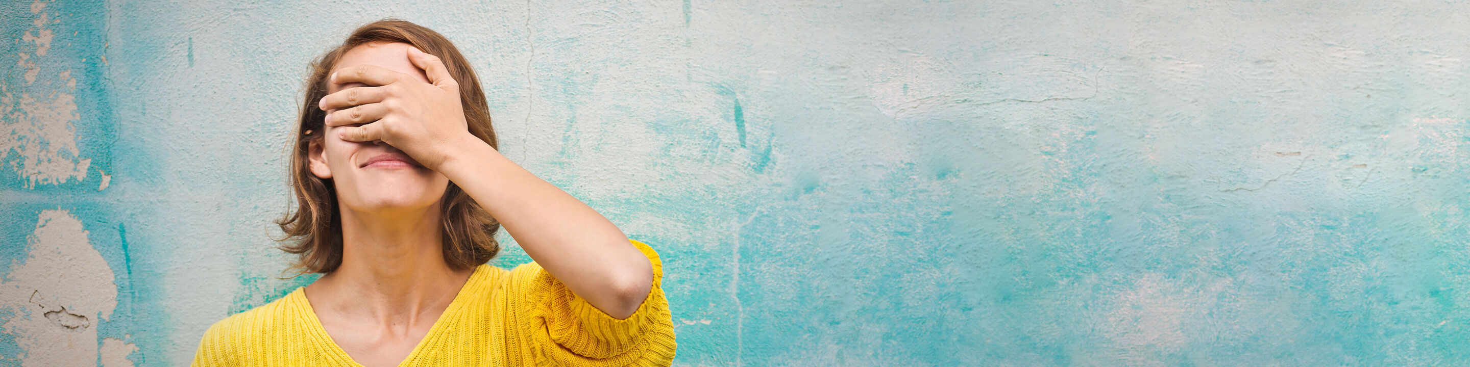 Une femme en pull jaune profite d'un moment de tranquillité devant un mur bleu.