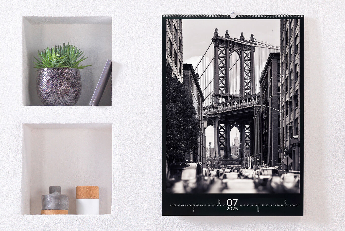 Un calendrier photo stylé est accroché à un mur. Juillet 2025 est visible, avec le Brooklyn Bridge en noir et blanc.