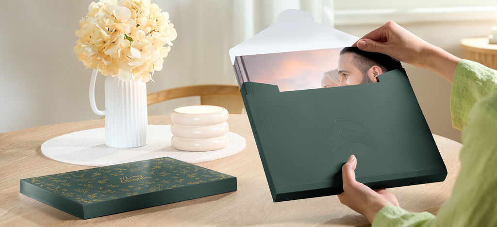 Une personne ouvre une jolie boîte-cadeau avec un album photo. Des fleurs et des éléments décoratifs créent une atmosphère chaleureuse.