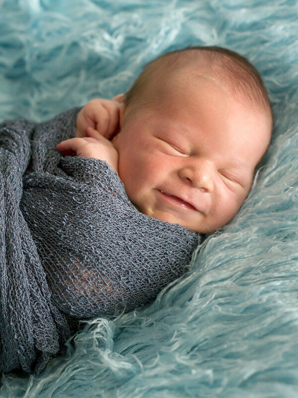 Un bébé emmailloté repose sur un fond turquoise doux. Le bébé s'emmitoufle dans la couverture.