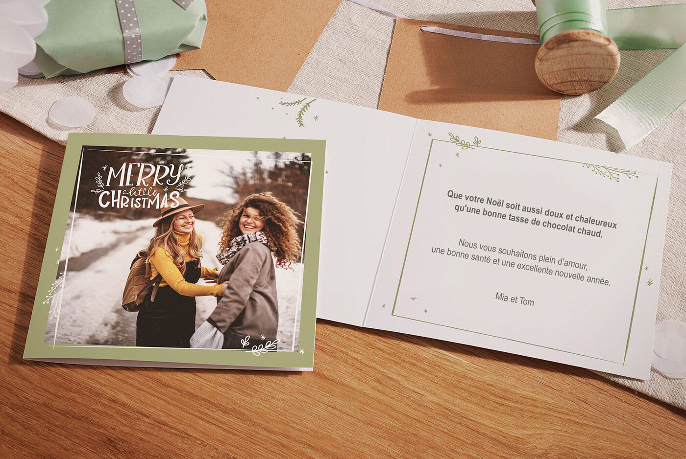 Une femme et un homme se tiennent sur un chemin enneigé. Ils rient et s'enlacent affectueusement. Des cadeaux et des décorations de Noël sont visibles en arrière-plan.