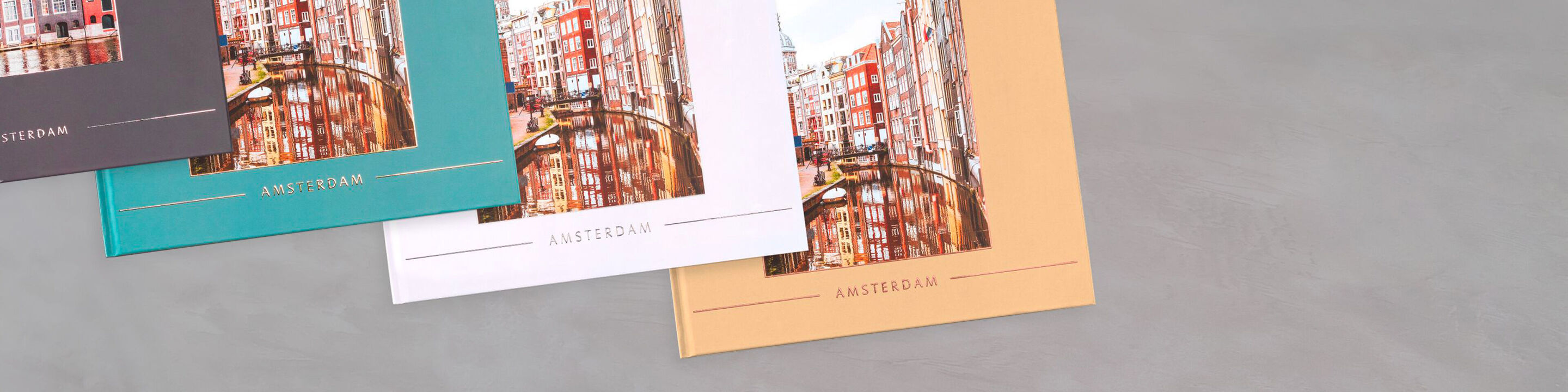 Trois livres photo CEWE colorés avec des motifs de villes sur un fond gris.
