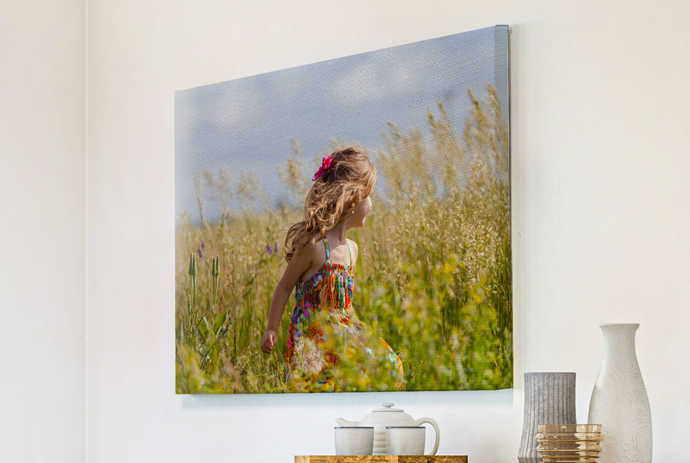 Une fille joyeuse avec des boucles blondes portant une robe colorée court à travers un champ fleuri.