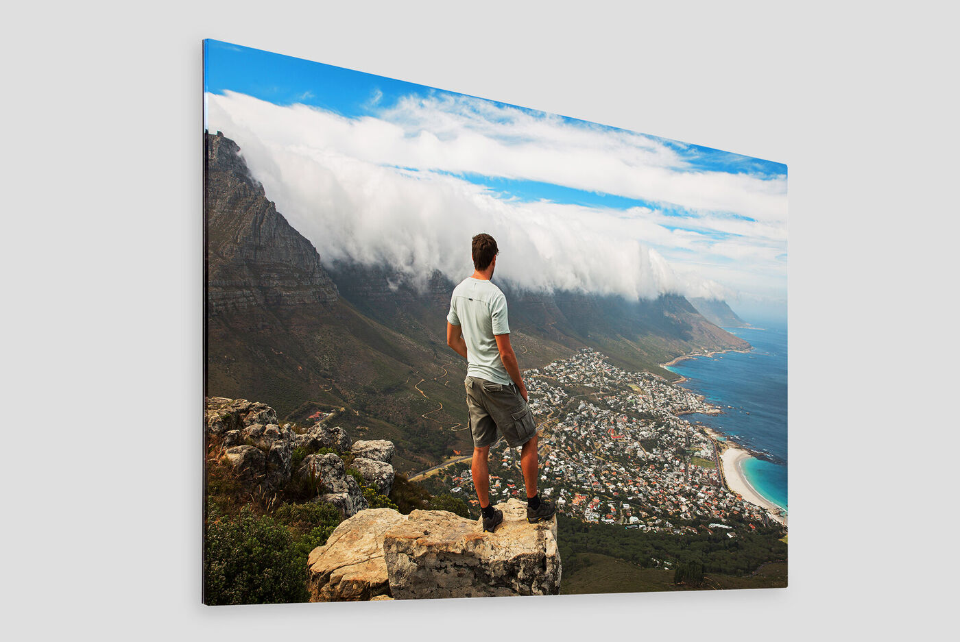 Homme se tenant sur un rocher avec vue sur la côte et les montagnes sous le ciel bleu