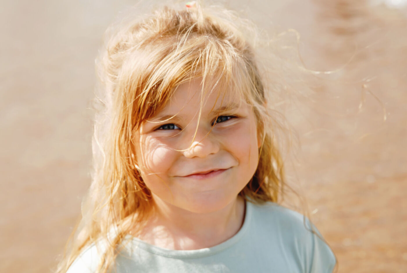 Enfant à la plage sous le soleil, cheveux blonds bouclés, souriant d'un air heureux