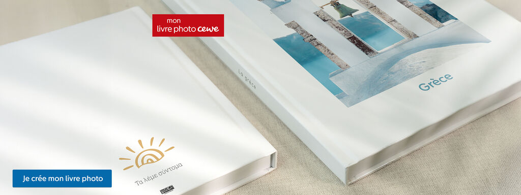 Deux albums photo CEWE sont sur une table. L'un montre une illustration ensoleillée, l'autre une image de Grèce.